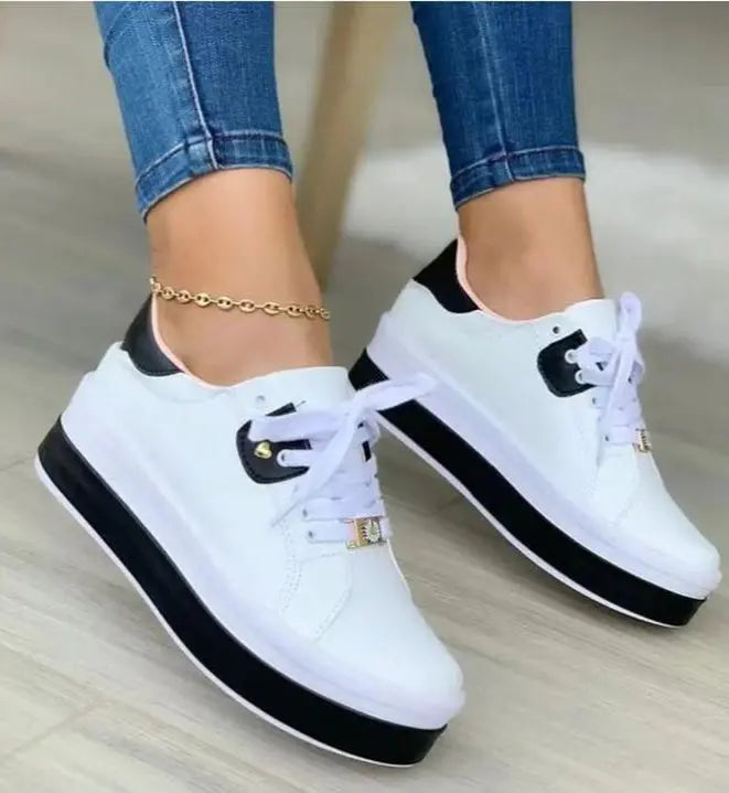 A pair of women's casual sneakers with white uppers and black accents, featuring a lace-up closure and a flat sole.