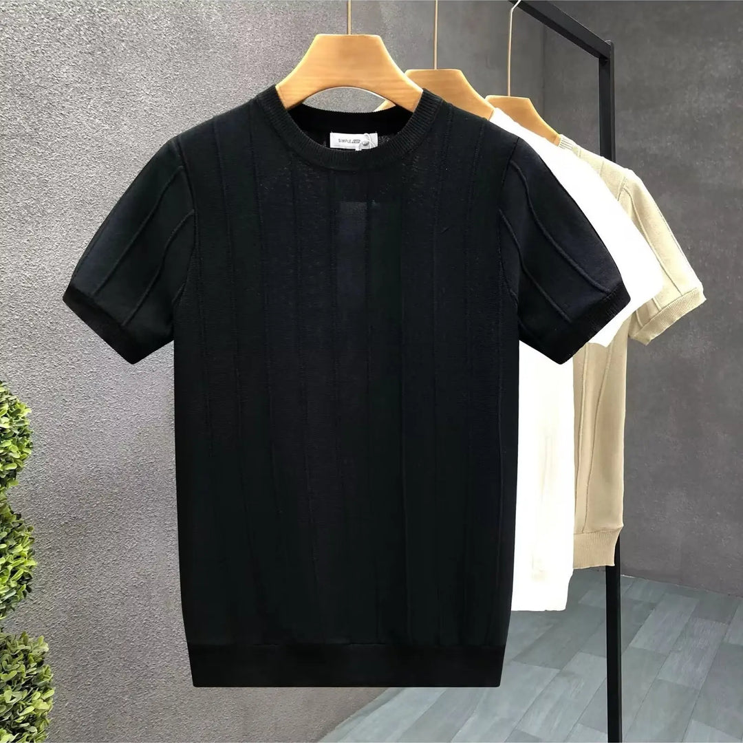 Black t-shirt on a hanger against a gray wall with a white t-shirt in the background.