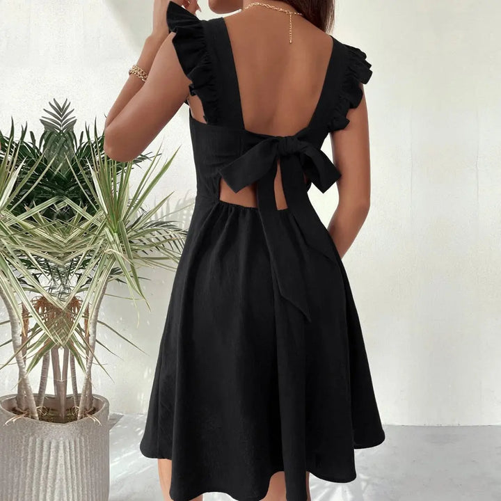 A woman wearing a black sleeveless knee-length dress with ruffled shoulder straps.