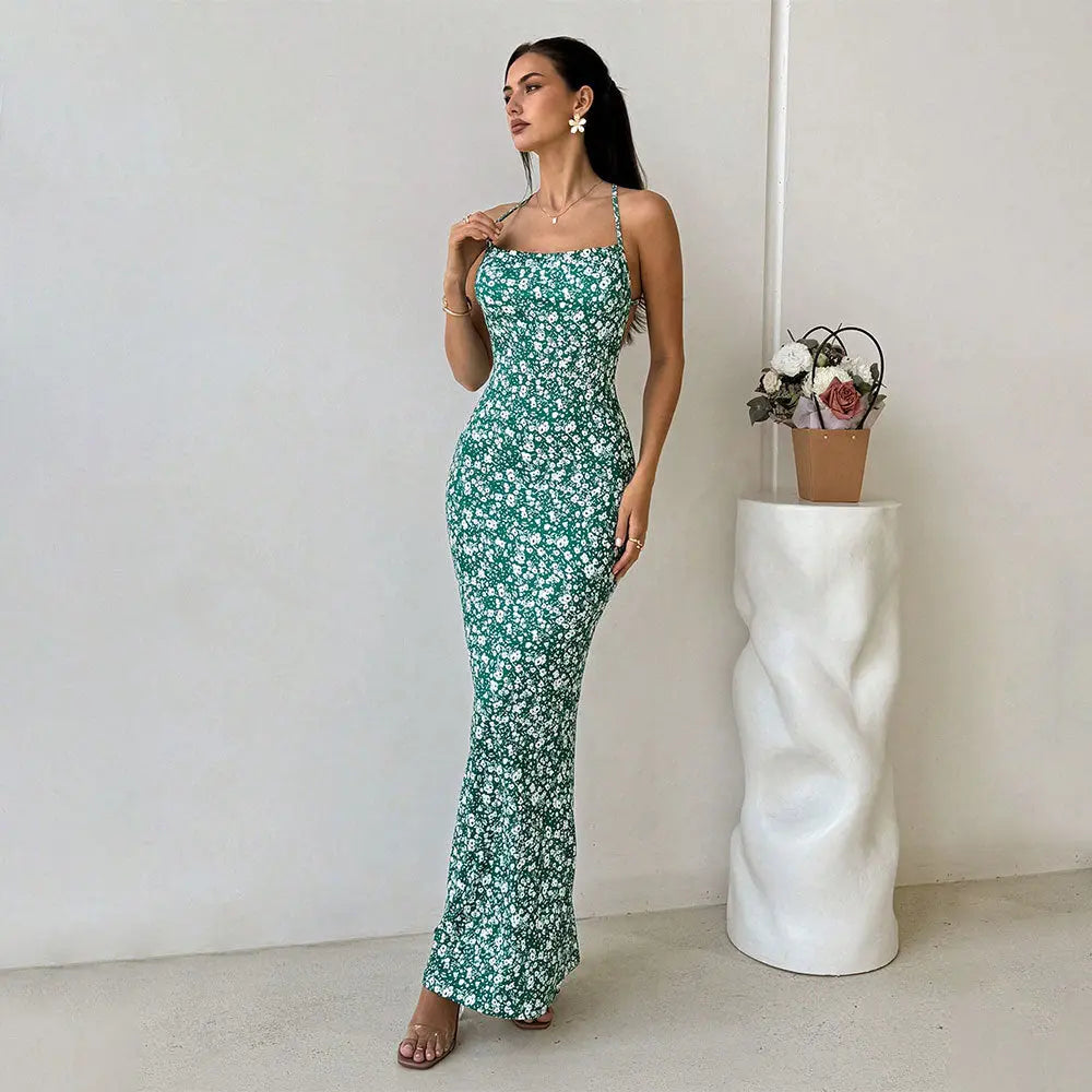 A woman wearing a sleeveless, green floral print, maxi dress with spaghetti straps