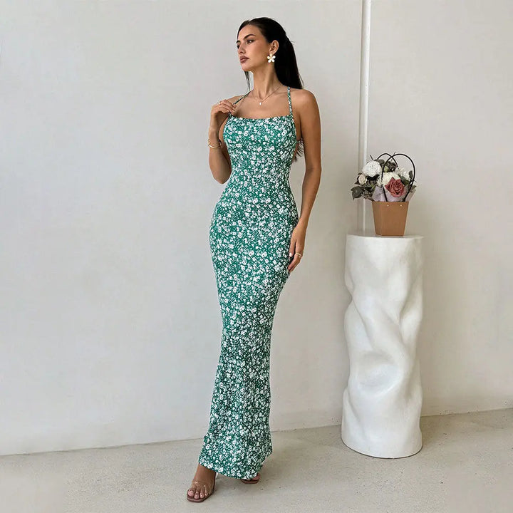A woman wearing a sleeveless, green floral print, maxi dress with spaghetti straps