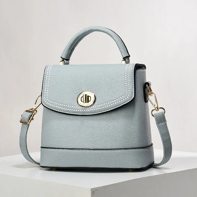 Elegant light blue faux leather top handle bag with gold twist-lock closure and rhinestone trim, perfect for casual or office wear.