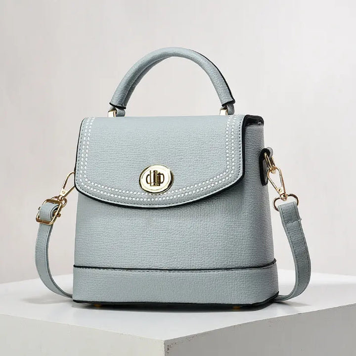Elegant light blue faux leather top handle bag with gold twist-lock closure and rhinestone trim, perfect for casual or office wear.