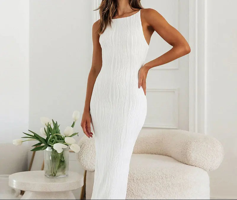 A woman wearing a white sleeveless maxi dress with a high neckline and ruffled hem.