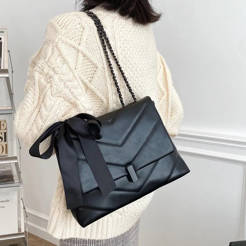 Stylish black quilted shoulder bag for women with chain strap and decorative bow, ideal for evening or date night looks.