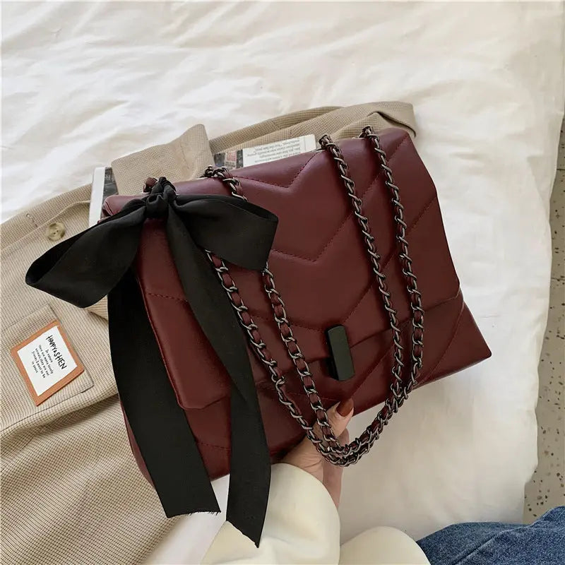 Stylish brown quilted shoulder bag for women with chain strap and decorative bow, ideal for evening or date night looks.