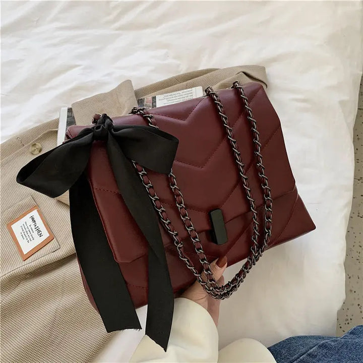 Stylish brown quilted shoulder bag for women with chain strap and decorative bow, ideal for evening or date night looks.