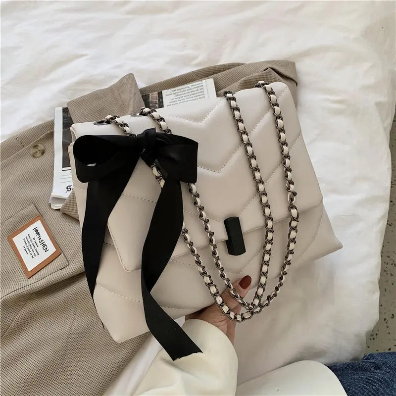 Stylish white quilted shoulder bag for women with chain strap and decorative bow, ideal for evening or date night looks.