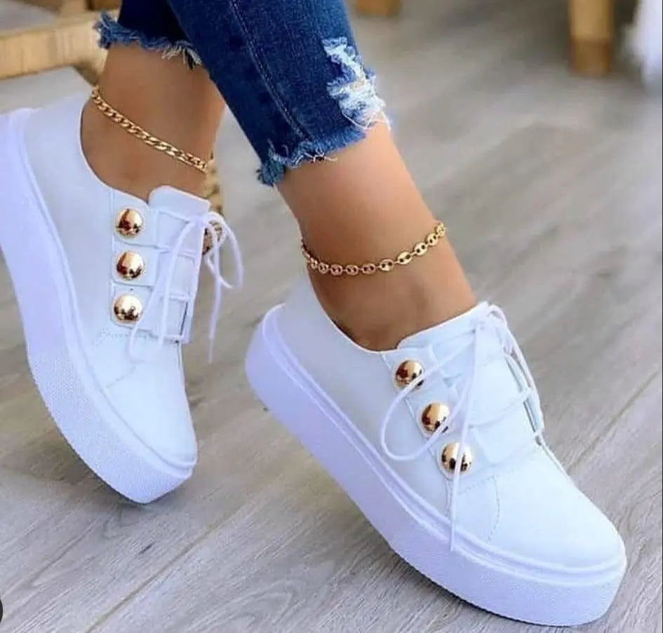White sneakers with gold buttons worn on a light wooden floor.