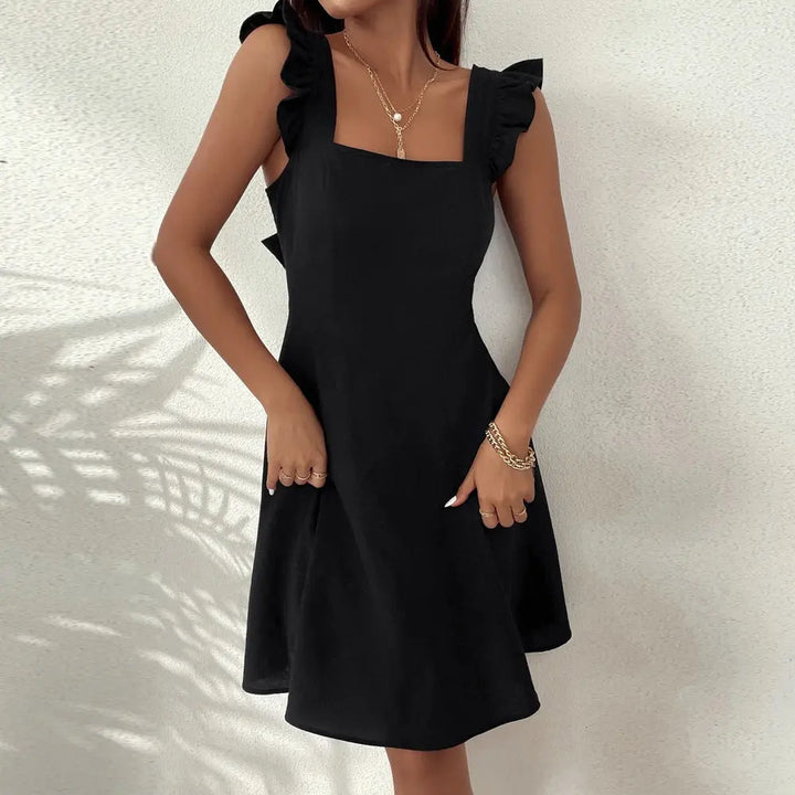 A woman wearing a black sleeveless knee-length dress with ruffled shoulder straps.