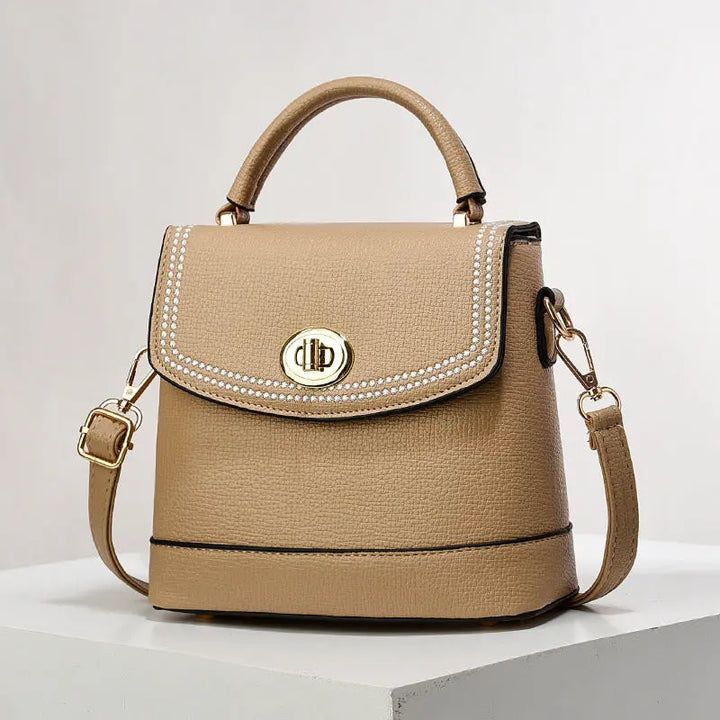 Elegant beige faux leather top handle bag with gold twist-lock closure and rhinestone trim, perfect for casual or office wear.