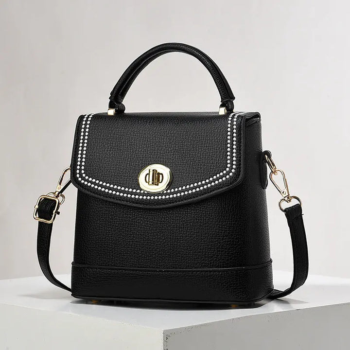Elegant black faux leather top handle bag with gold twist-lock closure and rhinestone trim, perfect for casual or office wear.