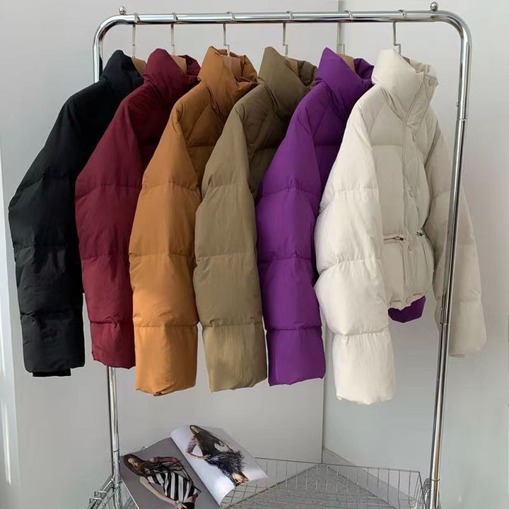 Row of colorful puffer jackets on a metal rack against a white wall.