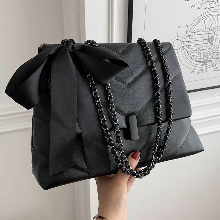 Stylish black quilted shoulder bag for women with chain strap and decorative bow, ideal for evening or date night looks.
