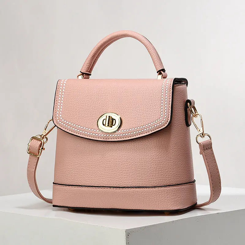 Elegant peach faux leather top handle bag with gold twist-lock closure and rhinestone trim, perfect for casual or office wear.