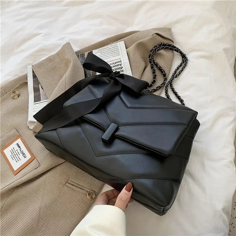 Stylish black quilted shoulder bag for women with chain strap and decorative bow, ideal for evening or date night looks.