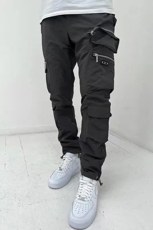 A pair of men's casual black trousers with multiple pockets and zippers, designed for versatility and functionality.