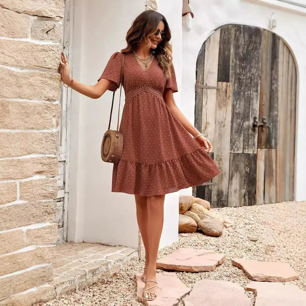 A woman wearing a brown, short-sleeve midi dress with a V-neckline and floral embroidery near the waist. 