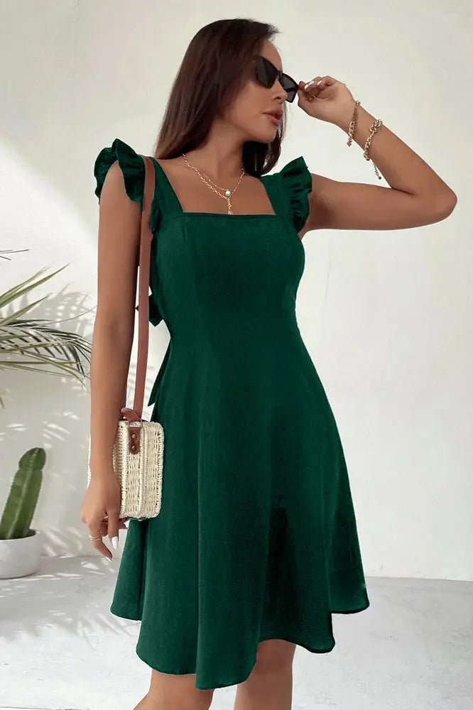 A woman wearing a green sleeveless knee-length dress with ruffled shoulder straps.